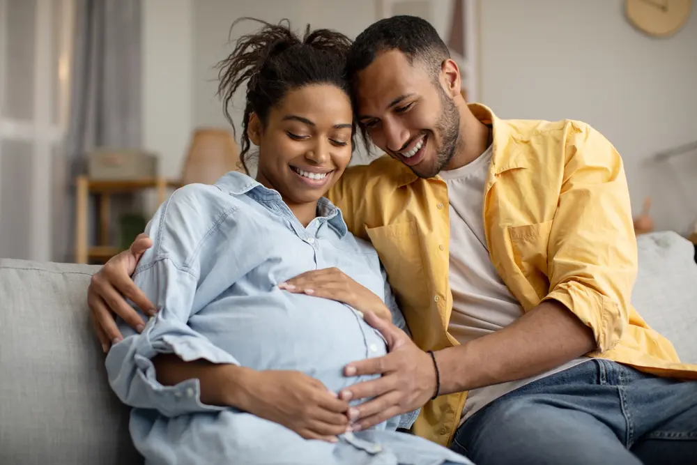 Pregnancy.,Black,Husband,And,Pregnant,Wife,Hugging,Sitting,At,Home.